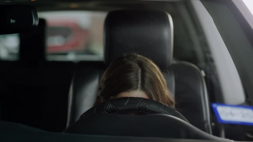 Woman startles awake in her car after napping with her head against the steering wheel