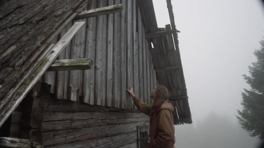 Man touches old wooden building with fog in background