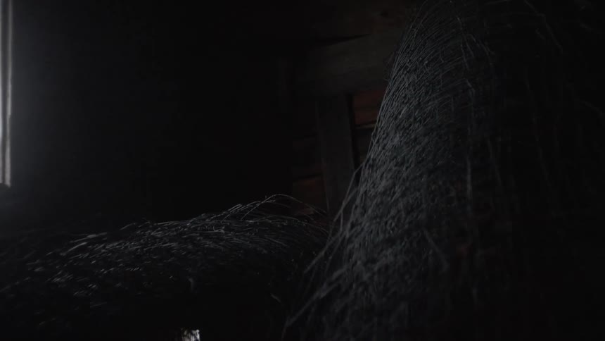 Camera shows dark insides of a some kind of a barn with piles of straw lying around