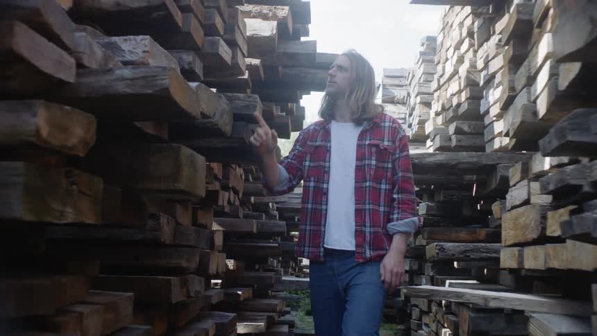 Man in flannel shirt walks through stacks of lumber