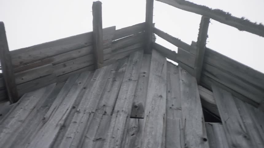 A wooden cabin missing planks from part of its roof