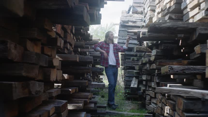 Man stands behind two walls of stacked wood beams and checks them