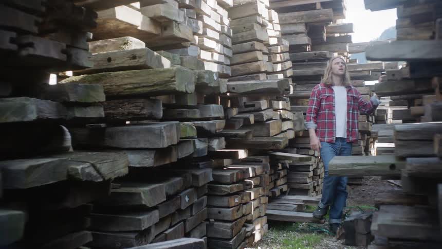 A man walks through a lumber yard and looks at the wood planks