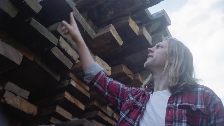 A man is choosing between planks of wood stacked to the sky