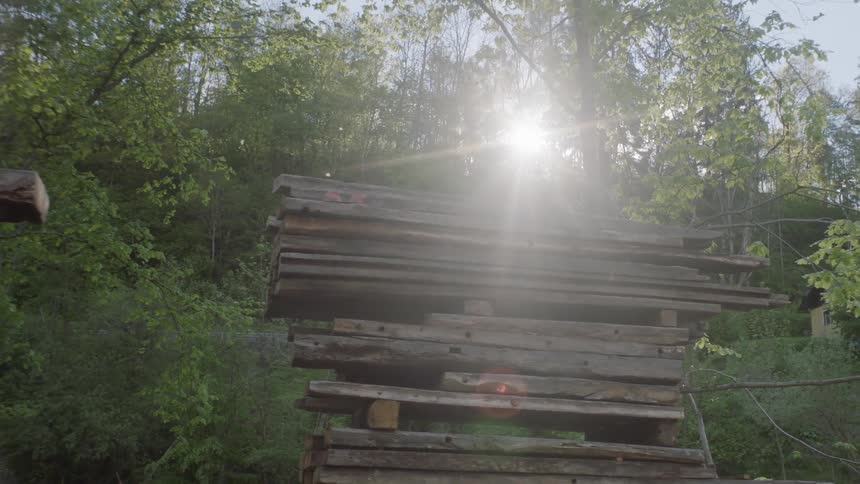 Darkened lumber stacked up on boards surrounded by trees and below a road