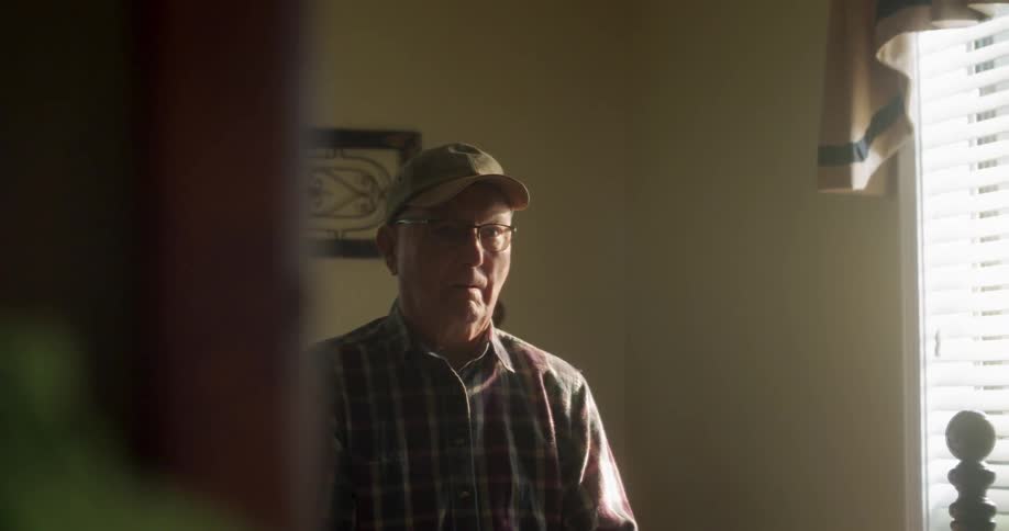 Old man sits and ponders in dimly lit bedroom