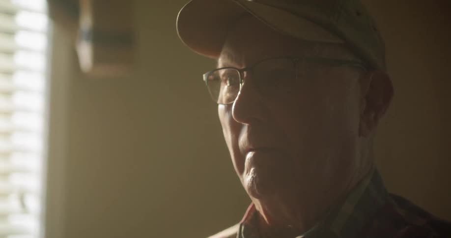 Older man looks up while sitting on bed