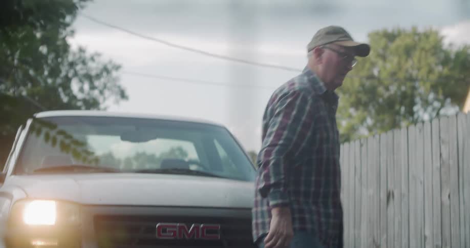 Man who wearing cap and striped shirt opens the wire fencing gate and returns to his car outdoors in the daytime