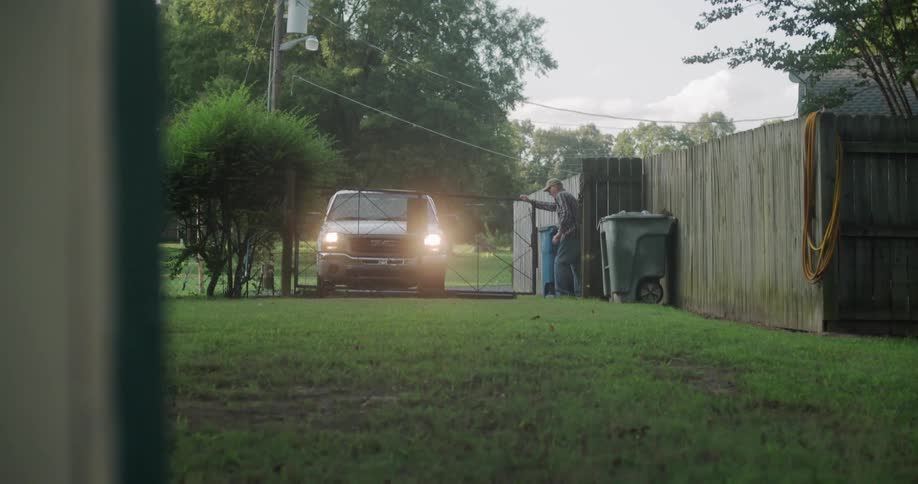 A man opens a fence to his yard in the country
