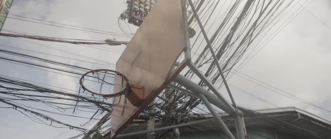 A broken basketball net stands under a large group of power lines
