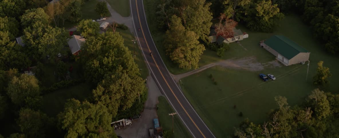 Motorcycles ride along road through rural community