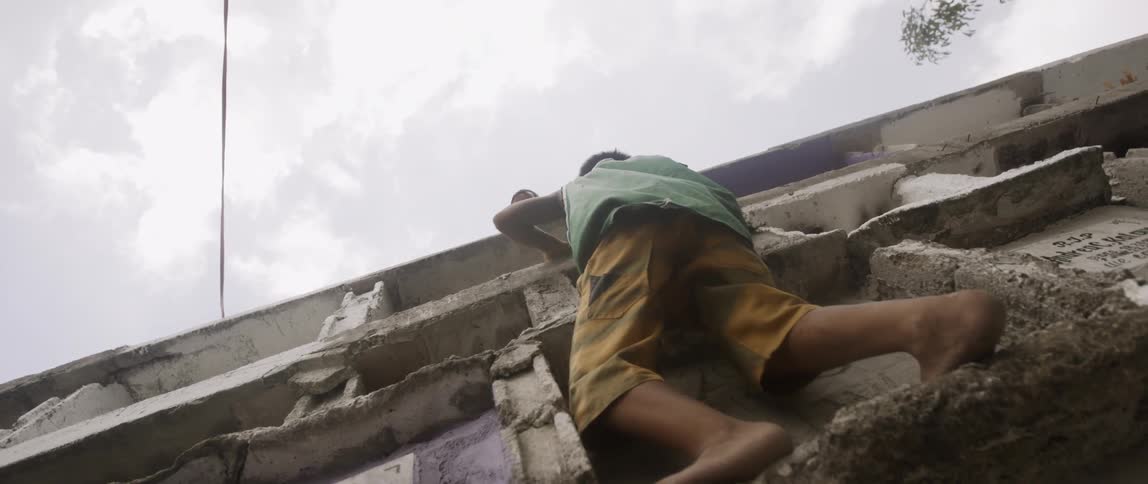 A boy climbing a concrete structure to reach another boy at the top