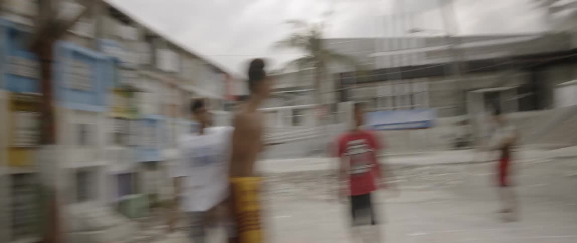 A group of boys play a game of basketball in a dirt lot