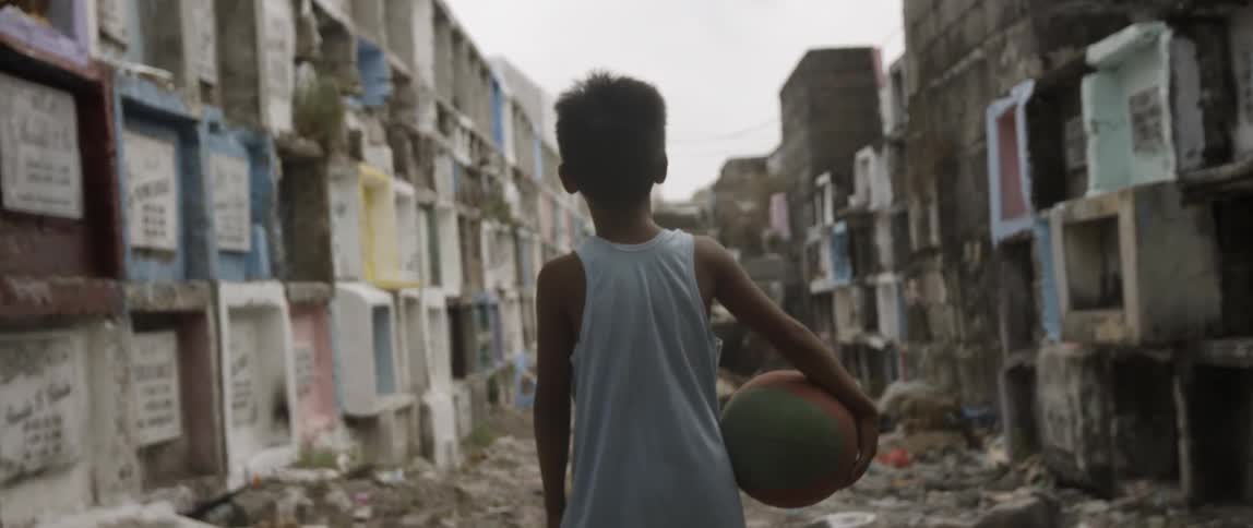 A boy is holding a ball in an alley on a cloudy day