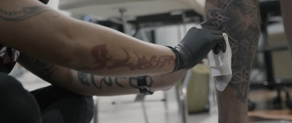 An asian man gives another man a tattoo