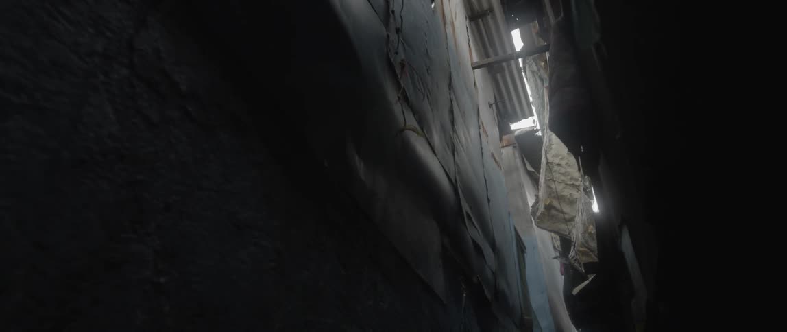 A claustrophobically narrow alley is filled with a variety of dangling debris wires and corrugated metal