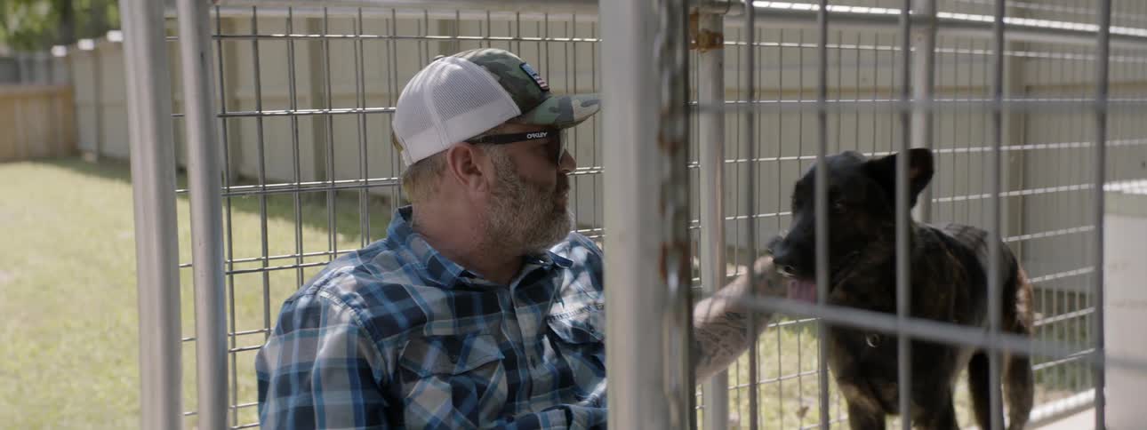Man petting and talking to a dog inside a cage