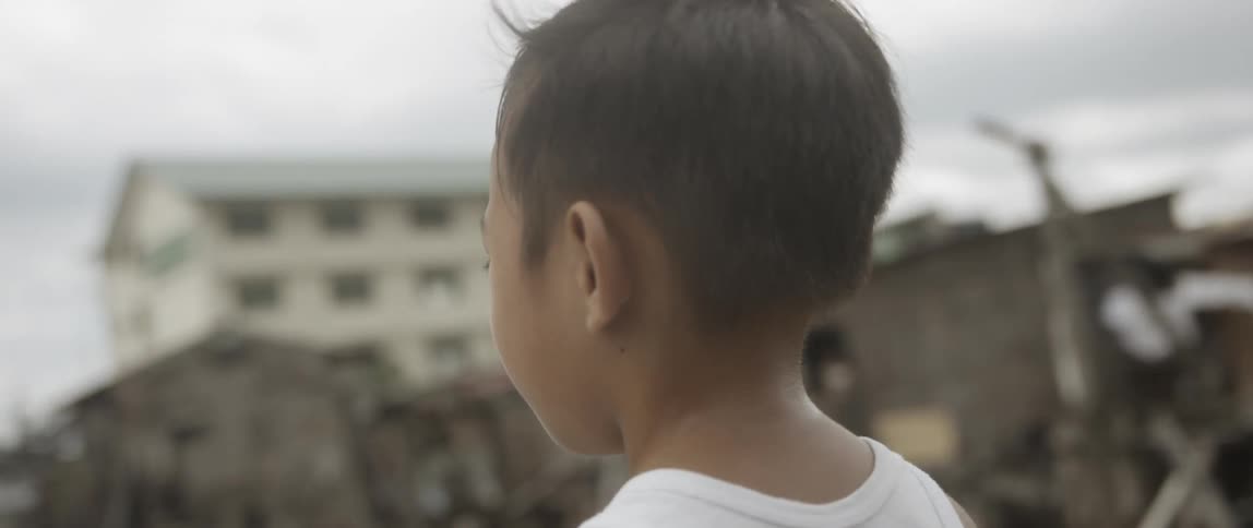 Boy stands among damaged and rickety buildings