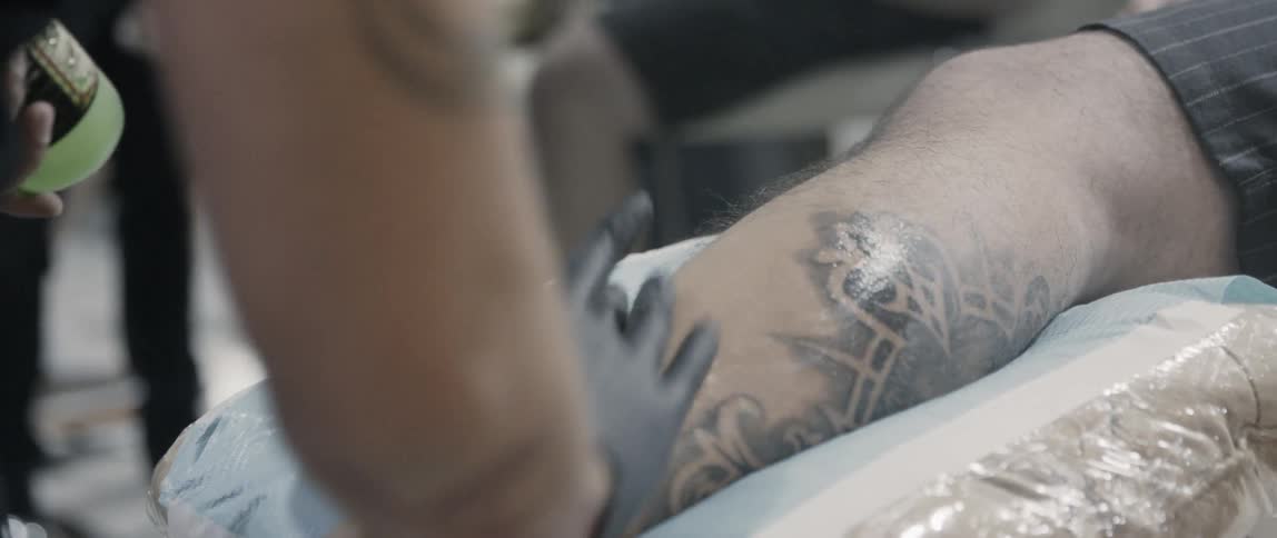 A tattoo artist smooths a gel onto a clients propped up leg