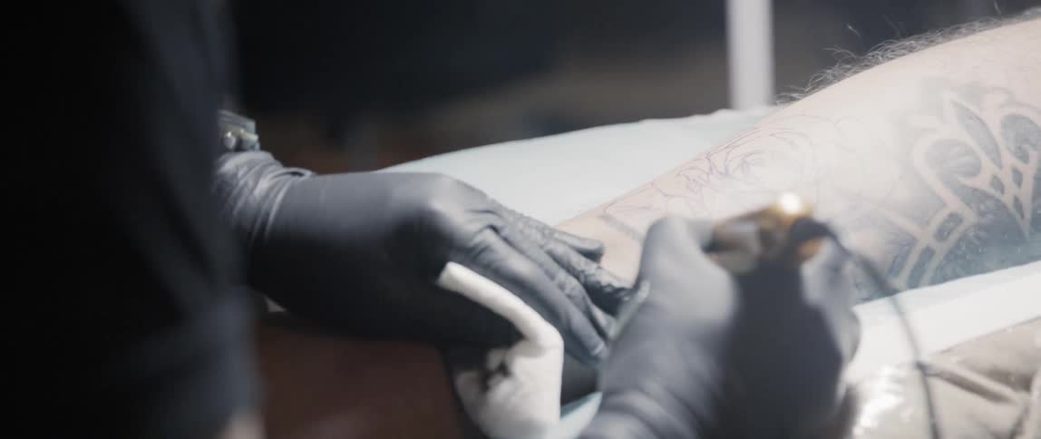 A tattooist is using a tattoo gun to apply ink to a man's lower leg