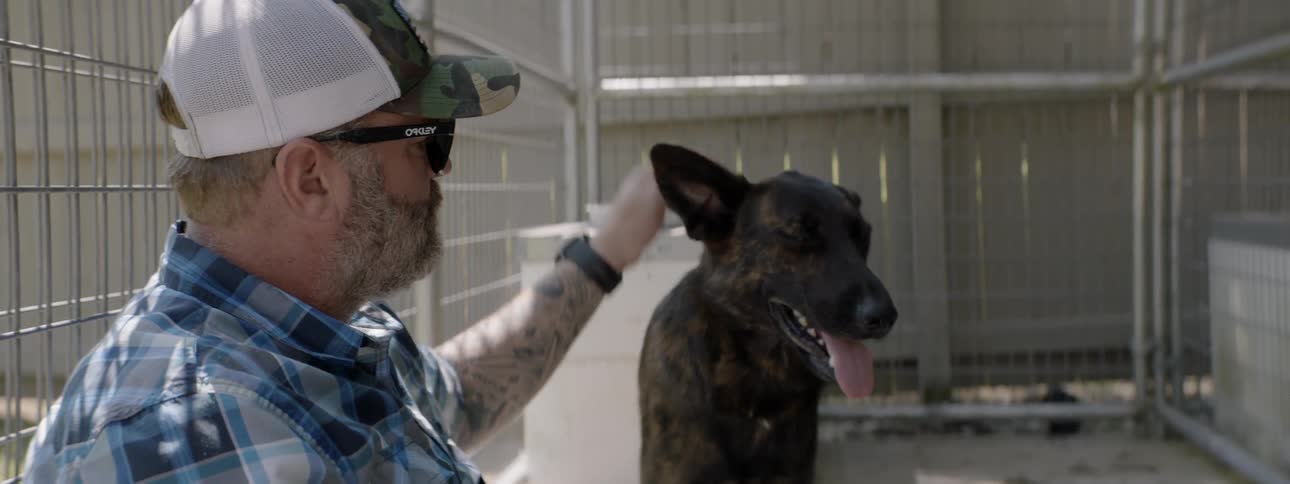 Man sitting inside a cage petting a black dog