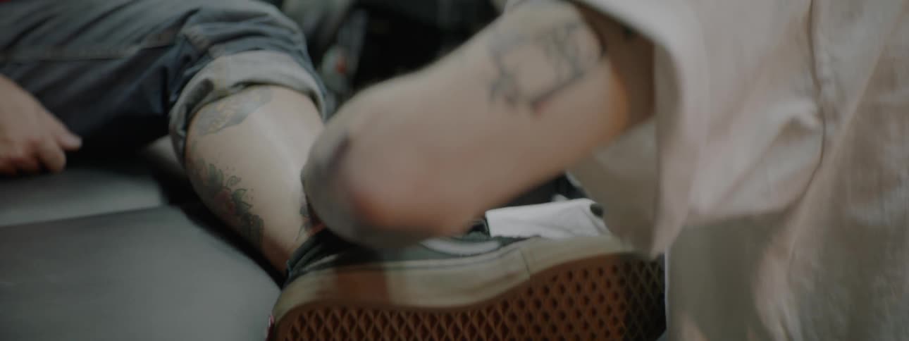 Tattoo artist tattooing a white mans leg sitting above a desk