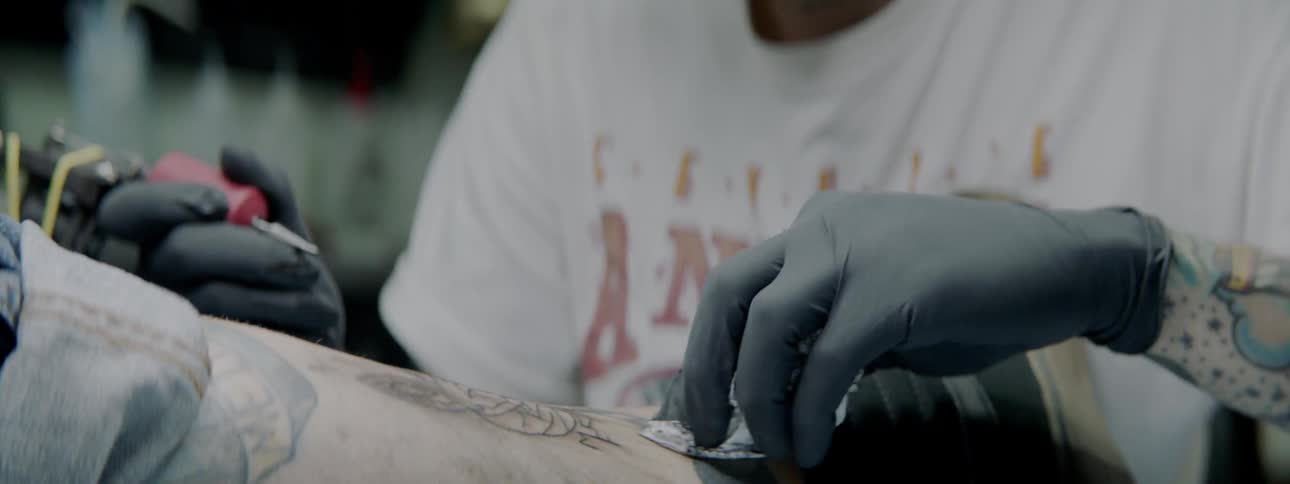 A male tattoo artist is inking a design on a customers leg