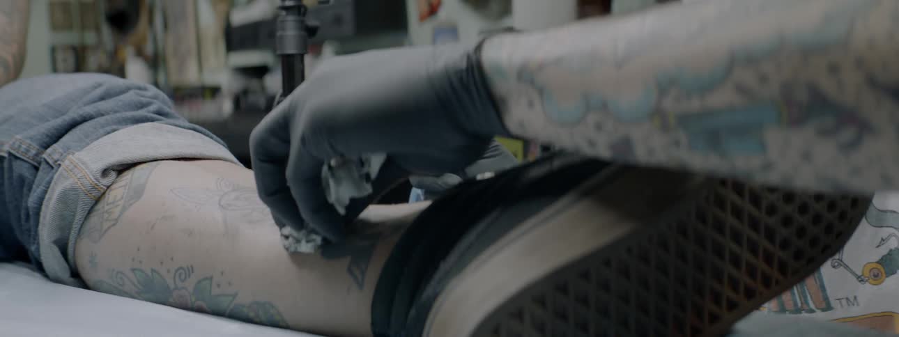 White man tattooing the leg of another white man
