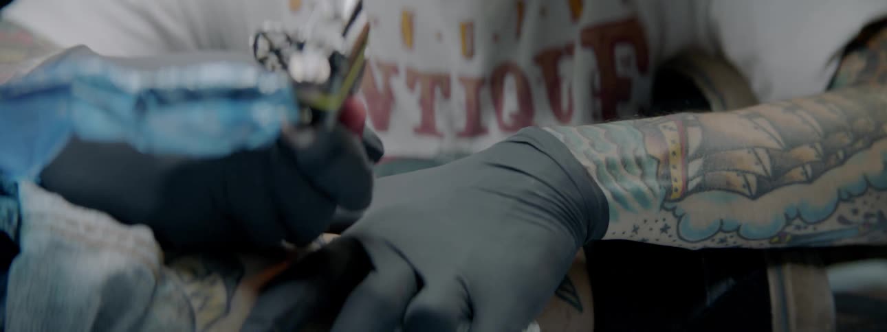 A young man smiles as he gives someone a tattoo
