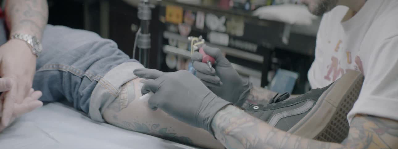 An older man is getting a tattoo on his left shin from a tattooist