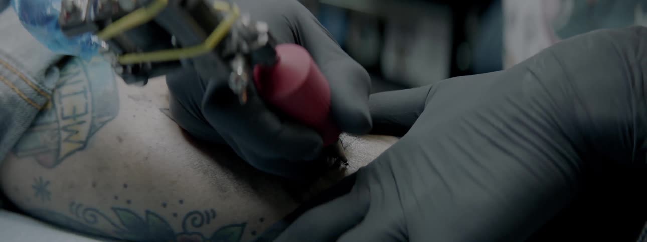 A tattooist works on a man