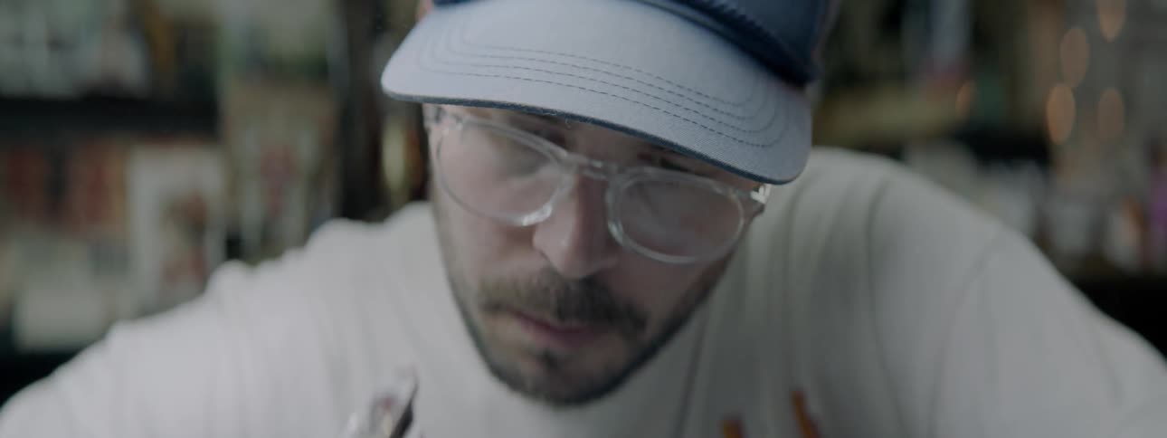 A tattoo artist wearing black gloves and a ball cap uses a tattoo gun to apply ink to a client