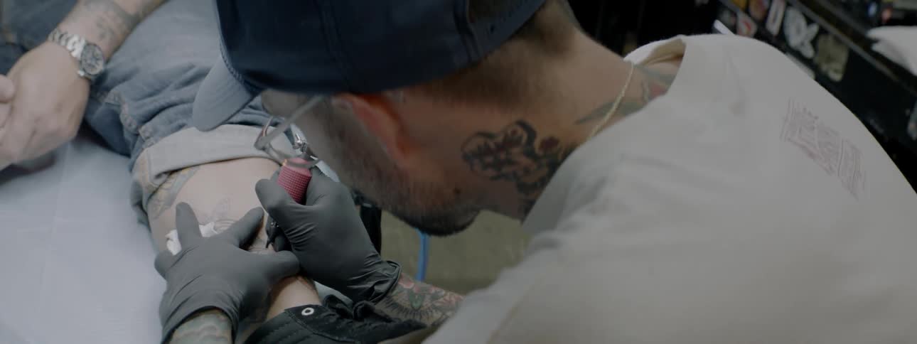 A tattoo artist tattoos a man's ankle in a shop