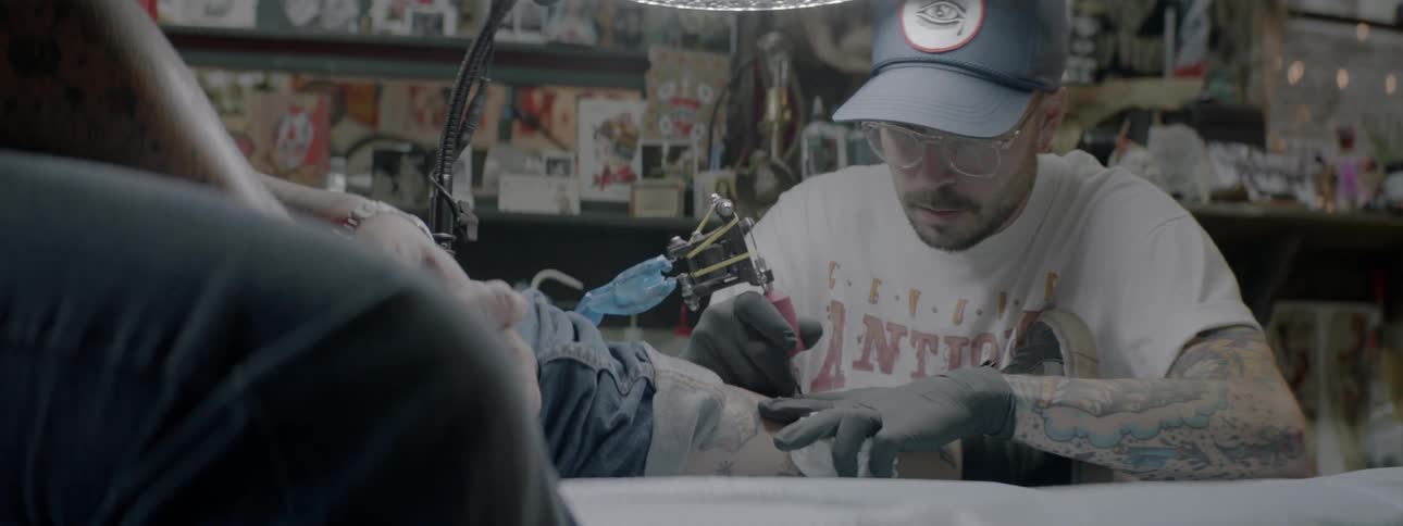 A tattoo artist tattoos a man's ankle in a tattoo shop