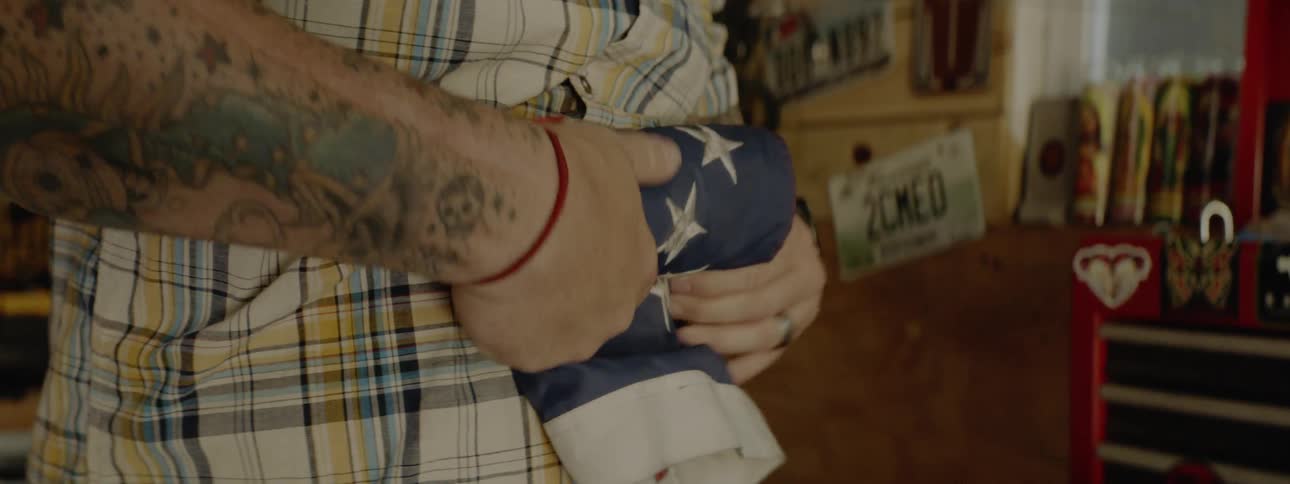 A man rolls an american flag up tightly while standing in a workshop near a toolbox