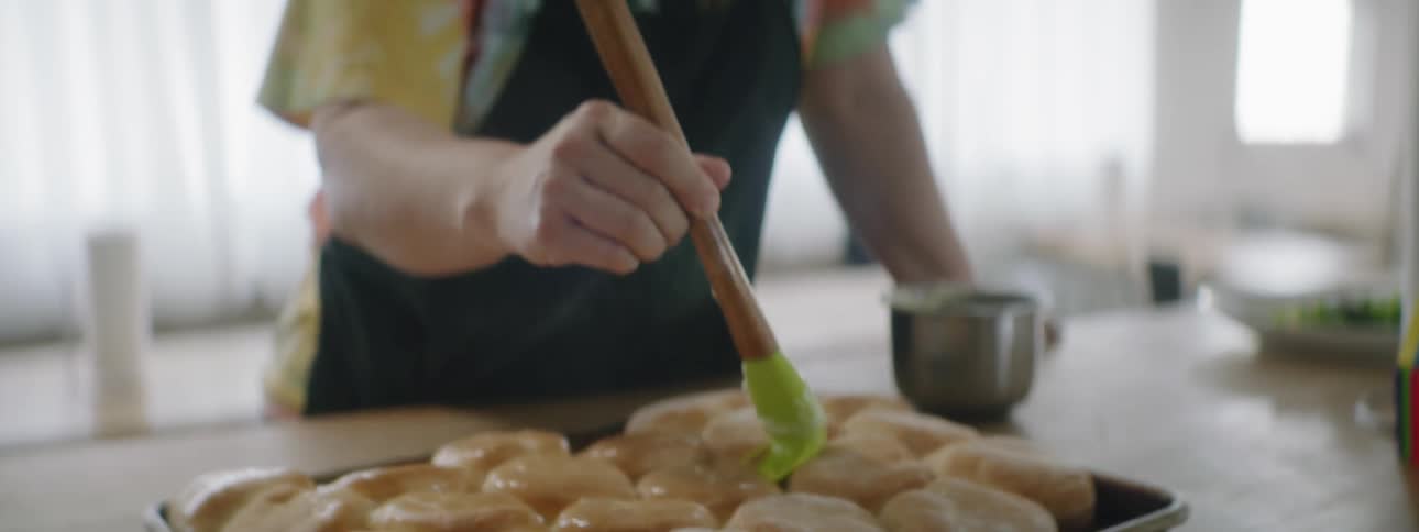 A woman is basting muffins in the pan