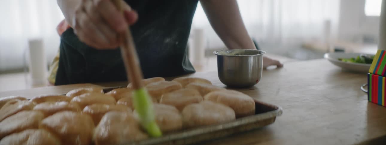 A woman is putting glaze on pastries