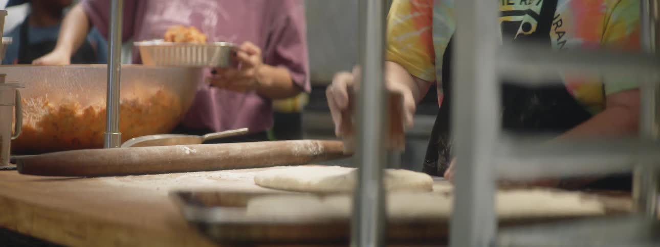 A baker uses a cup to cut a circle in dough then rubs the rim in flour