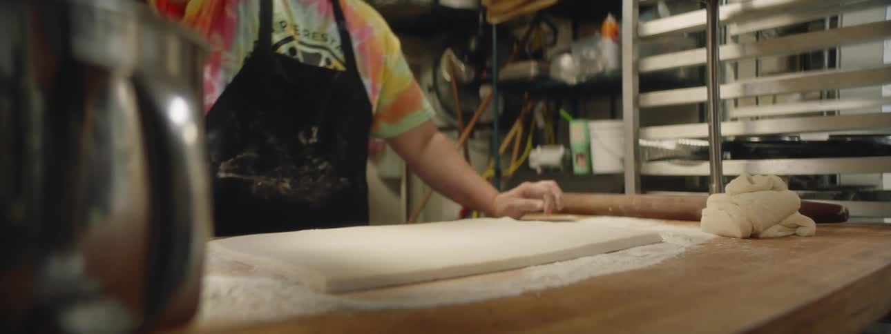 Baker sprinkling flour on flat shaped dough then spreading it around
