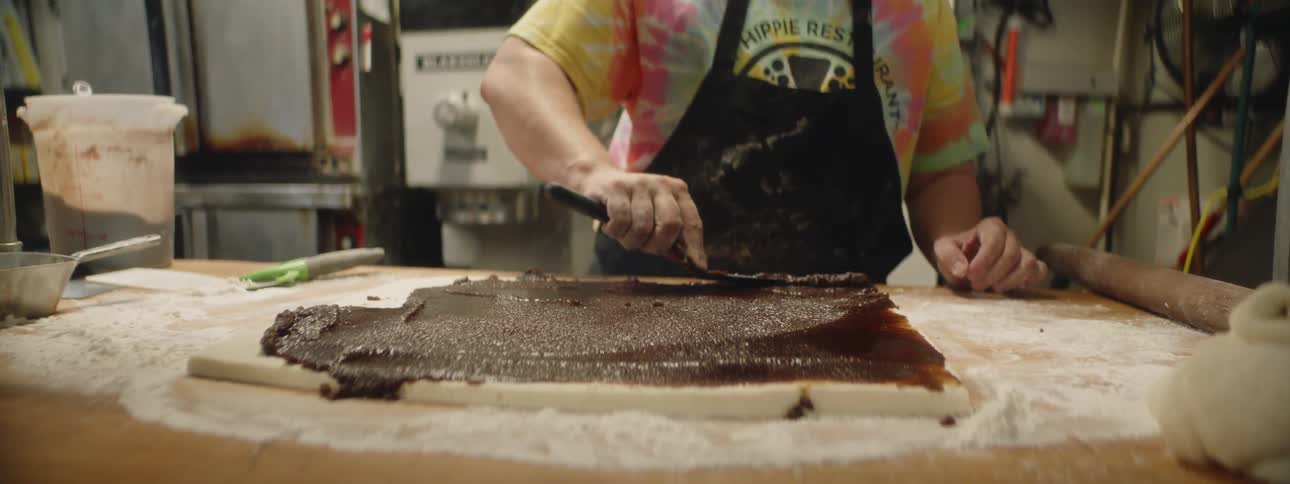 Woman spreads cinnamon paste on dough in commercial kitchen