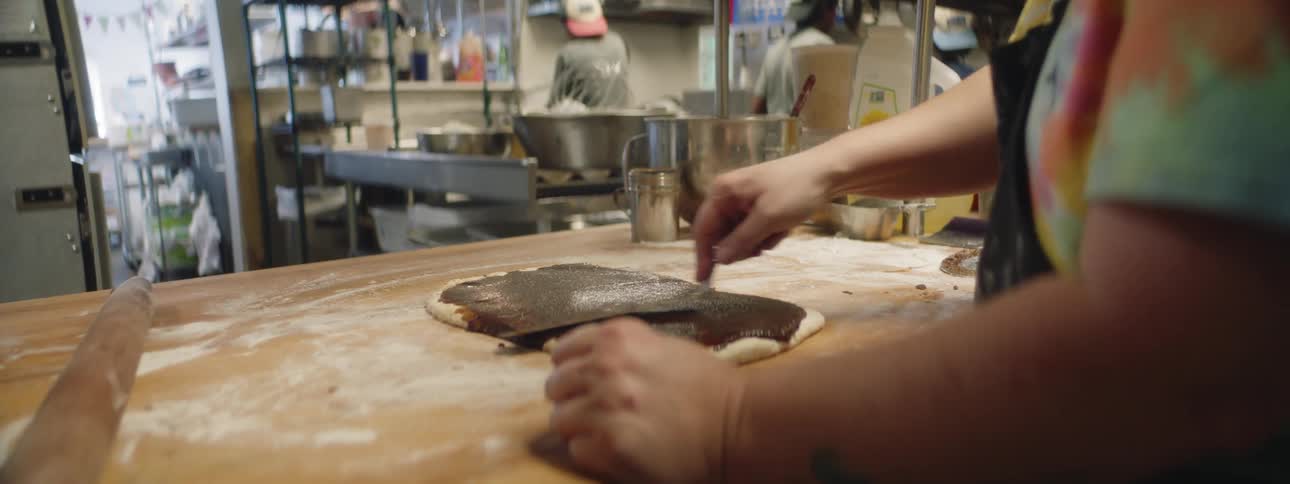 Woman with apron spreads chocolate on dough in the kitchen