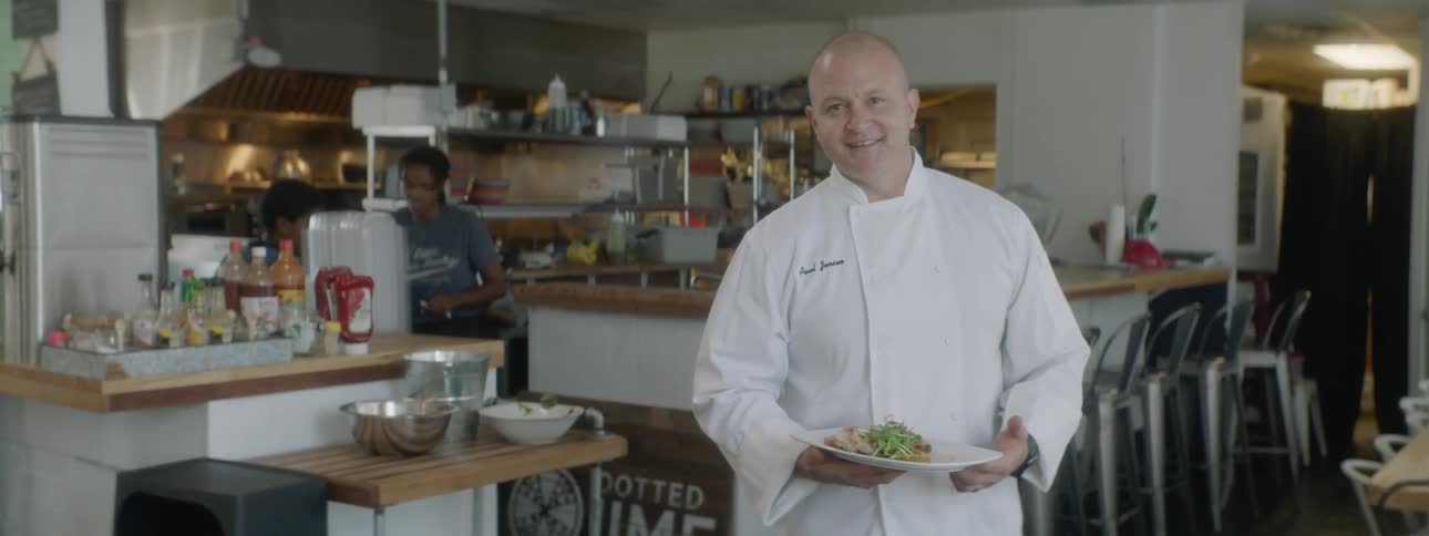 A chef holds a plate of food and smiles for the camera