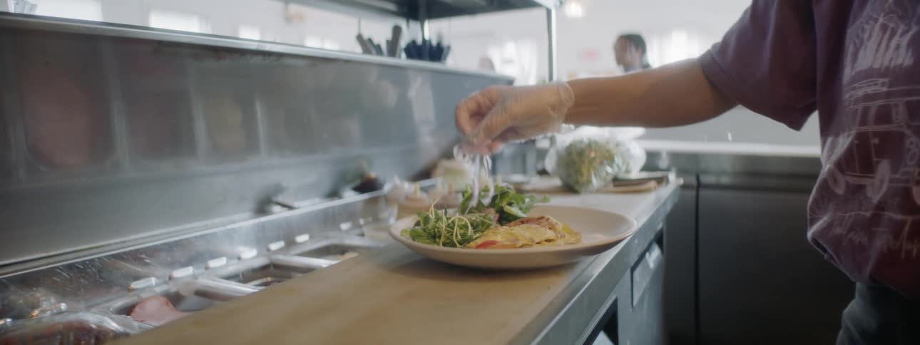 Cook puts some chopped onion on the plate next to the food in the kitchen during daylight