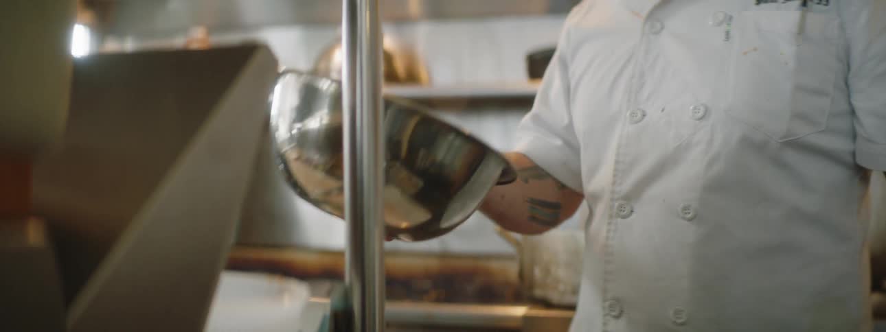 Chef flips ingredients in mixing bowl in commercial kitchen