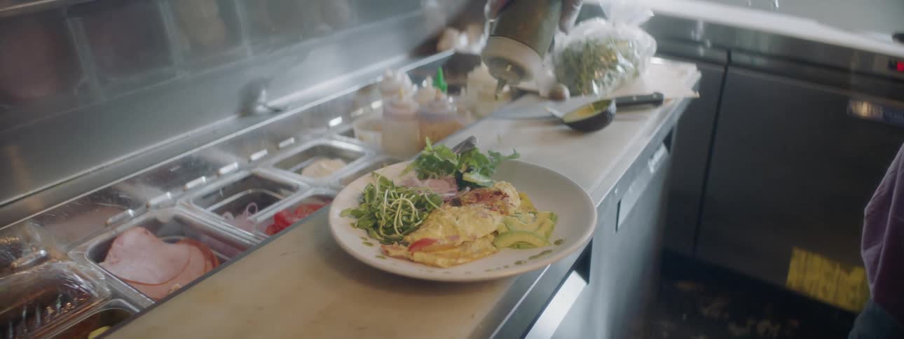 A cook squirts a condiment over a plate of food