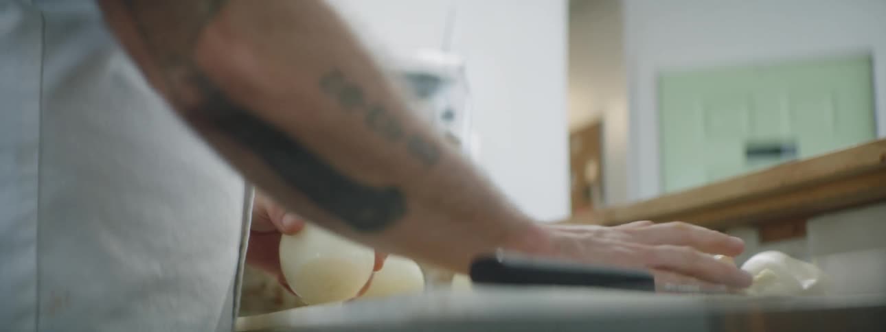 Tattooed man peels onion in the kitchen