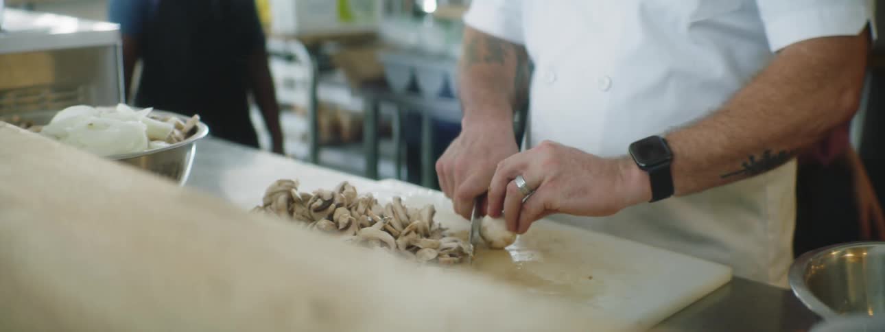 Man in chefs whites chopping mushrooms in a professional kitchen