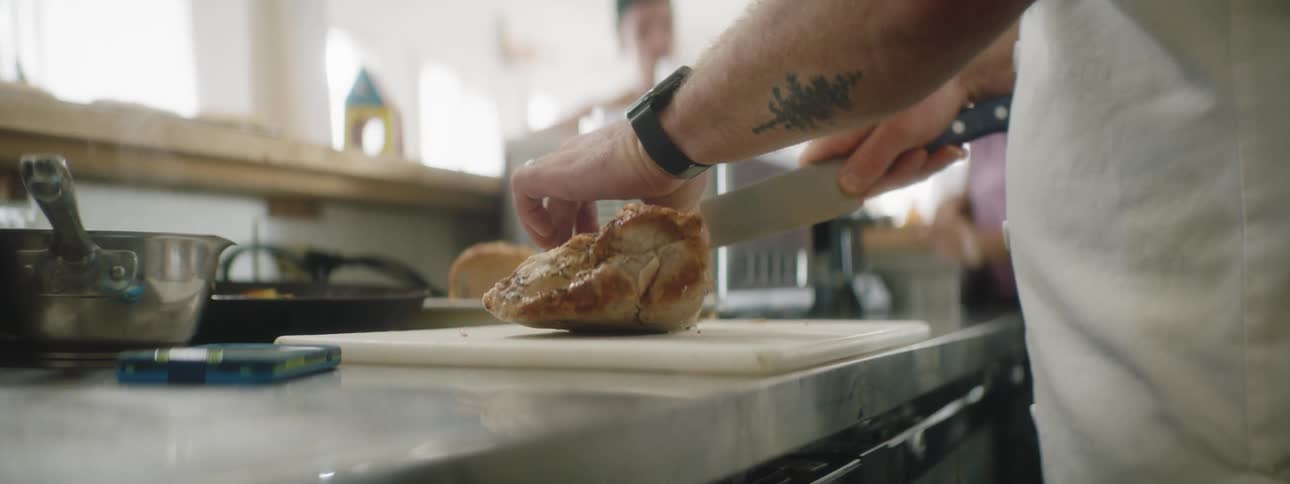 A man slices a chicken breast with a knife on a cutting board