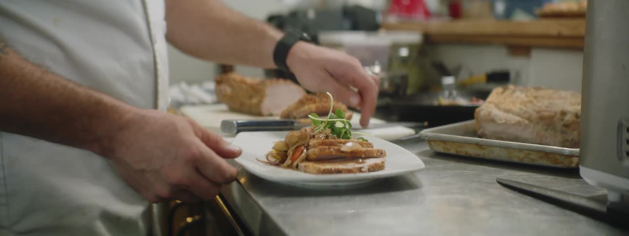 Tattooed man makes the last addition to the meal in the kitchen