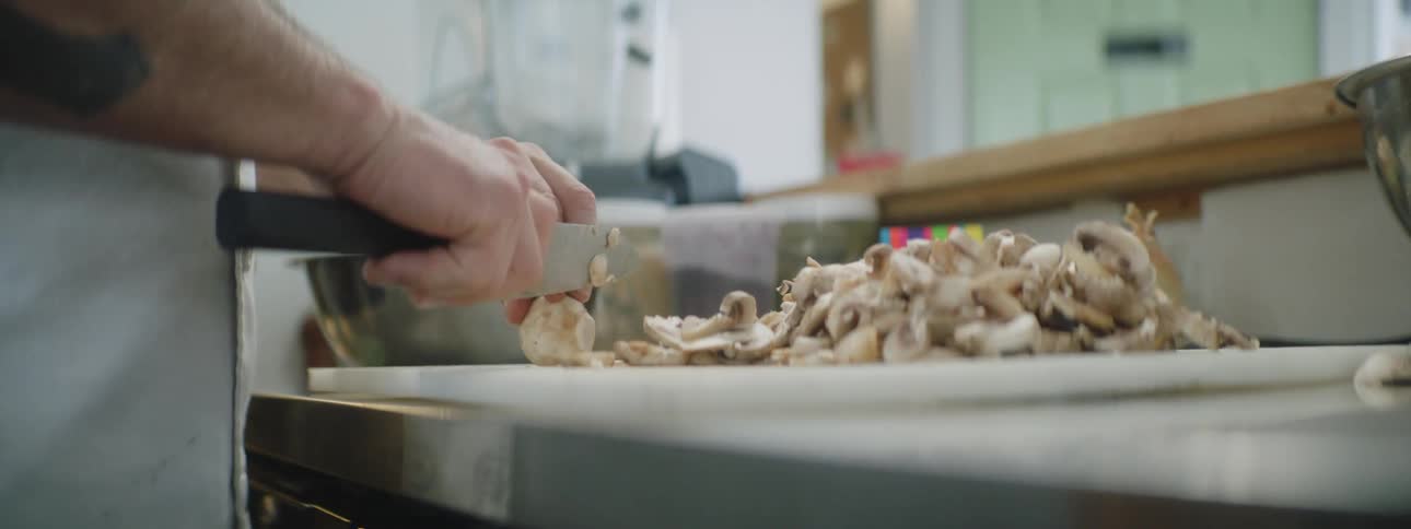 A man dices mushrooms on a cutting board in a home kitchen